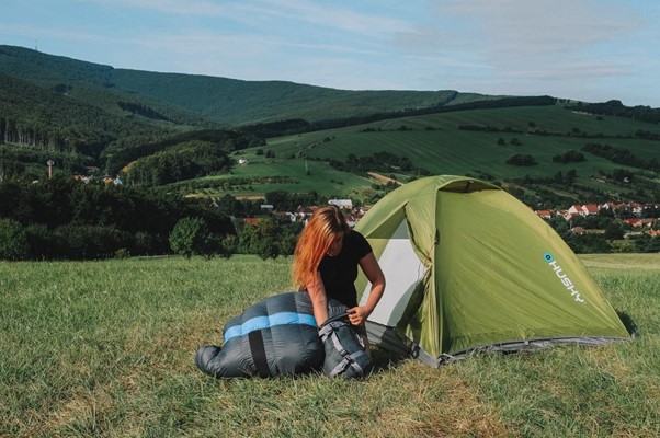 Střih i materiál spacáku vybírej podle toho, kam plánuješ vyrazit. Dívka se spacákem na louce u stanu